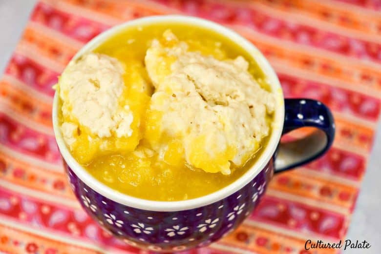 A close up shot of a mug of pumpkin soup topped with dumplings