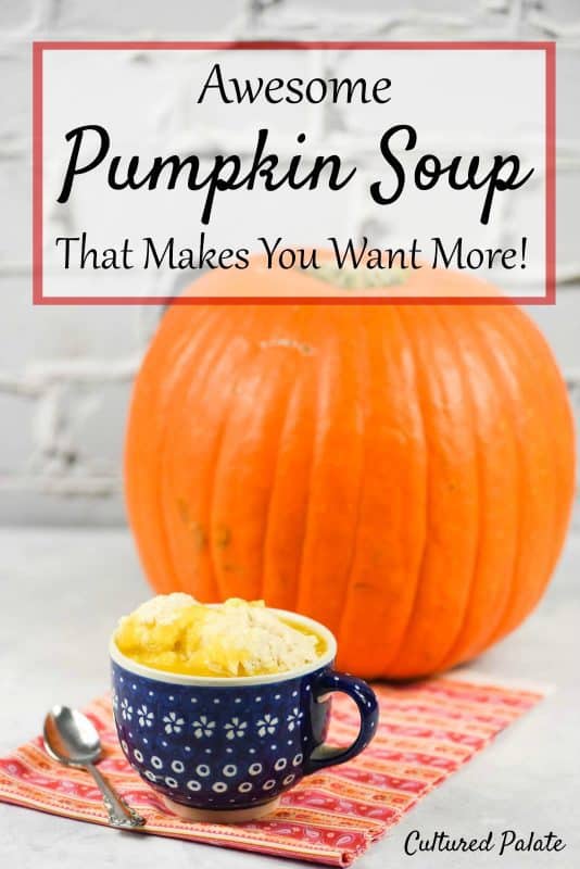 A large mug of pumpkin soup and dumplings sitting on a work surface with a pumpkin in the background