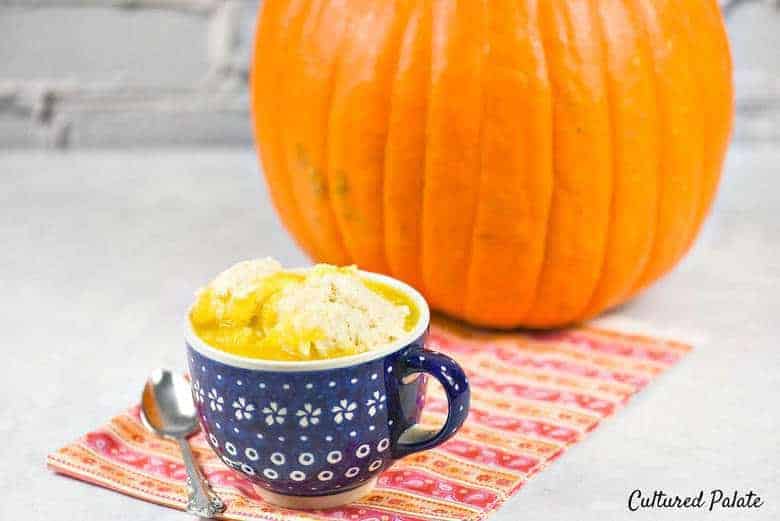 Pumpkin soup recipe - a mug of pumpkin soup topped with dumplings on a white surface