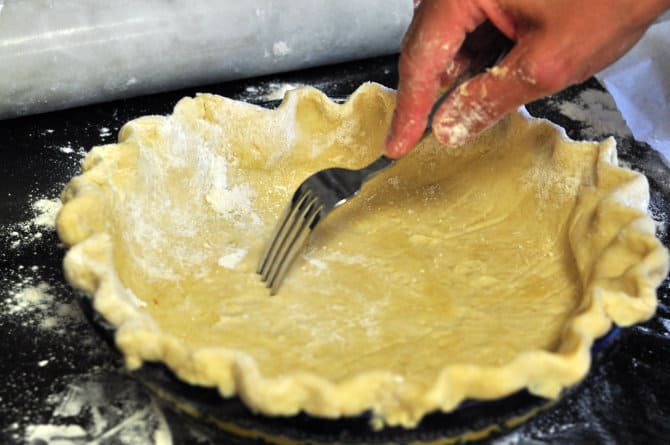 A fork pricking a homemade pie crust dough in a pie dish