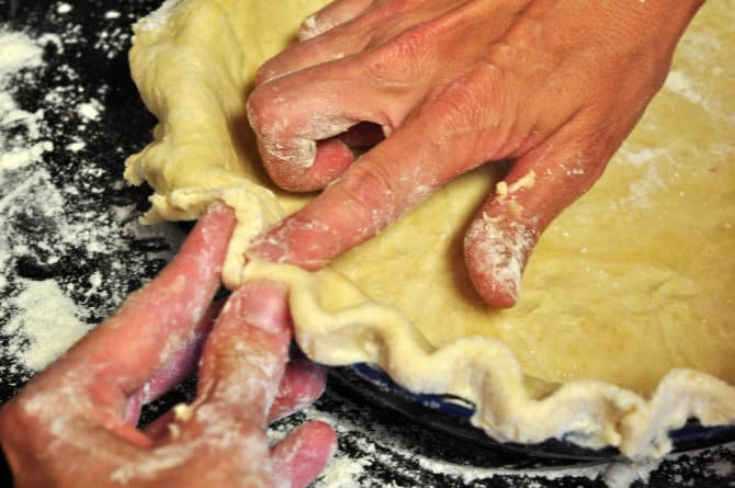 two hands shaping edges of a homemade pie crust