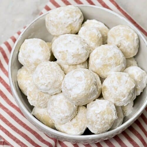 A white bowl of Italian Wedding cookies also known as Mexican Wedding Cookies on a red and white striped napkin.