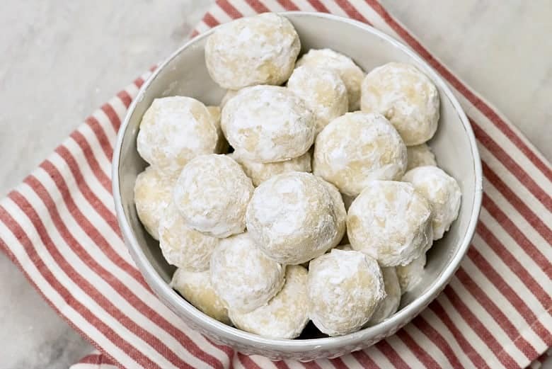A white bowl of Italian Wedding cookies also known as Mexican Wedding Cookies on a red and white striped napkin.