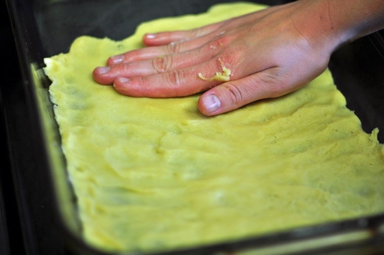 A hand patting pastry ingredients to make angle wings cookies into a tray