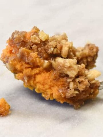 Sweet Potato Soufflé Recipe, also known as Sweet Potato Casserole recipe on a spoon. It has a brown sugar topping complete with nuts - its a delicious sweet potato recipe. #myculturedpalate #sweetpotatorecipe #sweetpotato #brownsugar #holiday