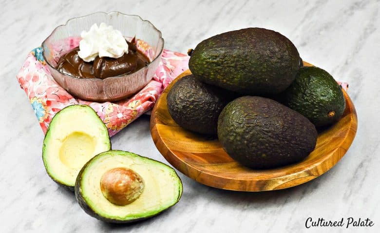 Chocolate Avocado Pudding  - a bowl of pudding with ripe avocados in a bowl and one cut open