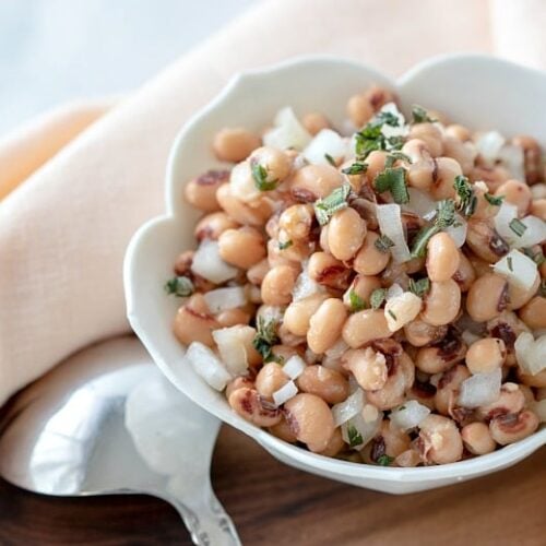 Black-Eyed Pea Salad shown in white bowl with spoon on wooden board.