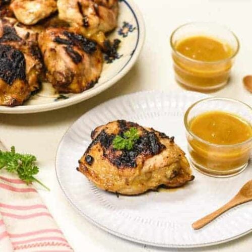 grilled chicken from the Honey Mustard Chicken recipe shown on a white plate with dipping sauce to the side and more chicken in the background