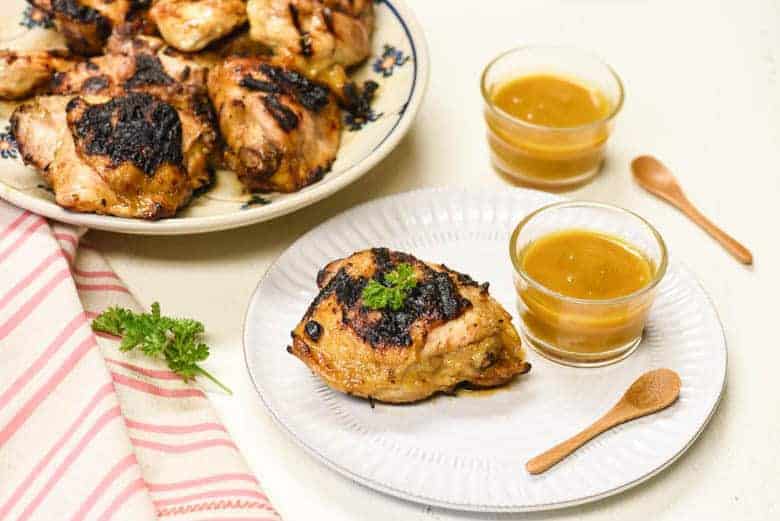 grilled chicken from the Honey Mustard Chicken recipe shown on a white plate with dipping sauce to the side and more chicken in the background