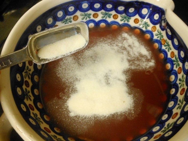 A spoon sprinkling gelatin into fruit juice to make homemade jello