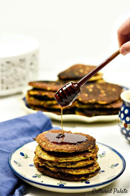 Butternut Squash Pancakes shown on plate with honey being drizzled over them.