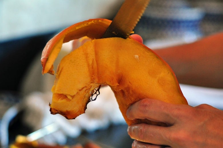 Squash cut into wedges that have been removed from the oven and in the process of cutting the skin off with a knife