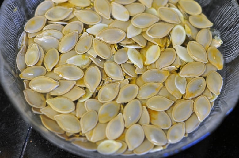 An overhead shot of pumpkin seeds in a large bowl soaking in water