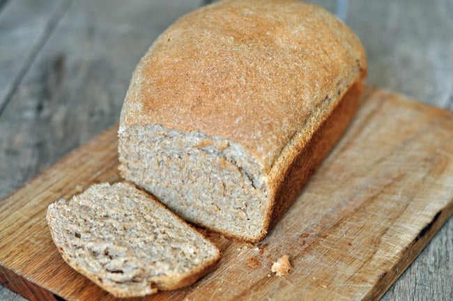 A close up shot of a Whole Wheat Bread loaf on a wooden chopping board with one slice cut