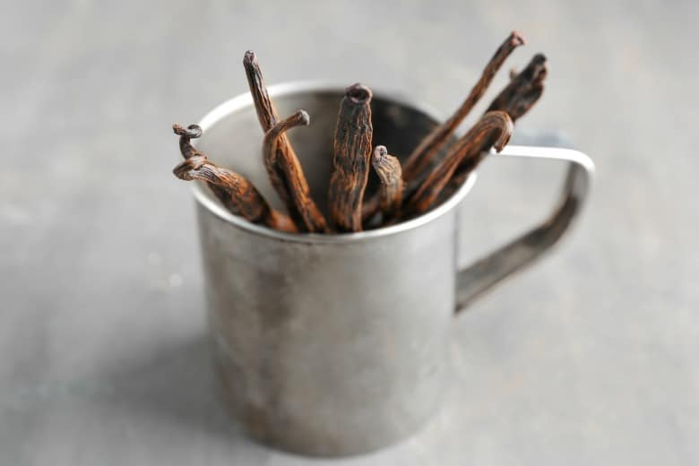 Vanilla beans shown in a metal cook on cement board.
