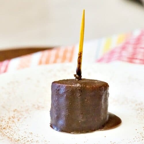 A single Chocolate Covered Banana Bite on a white plate with yellow toothpick and colorful napkin.