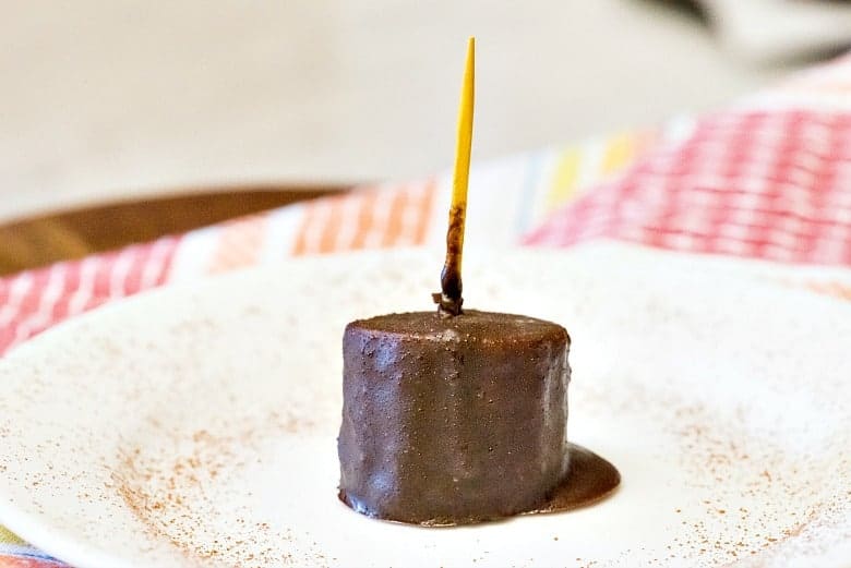 A single Chocolate Covered Banana Bite on a white plate with yellow toothpick and colorful napkin.
