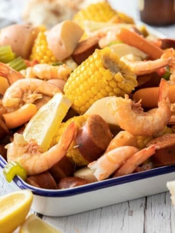 Shrimp boil recipe shown ready to eat in enamel container on wooden table.
