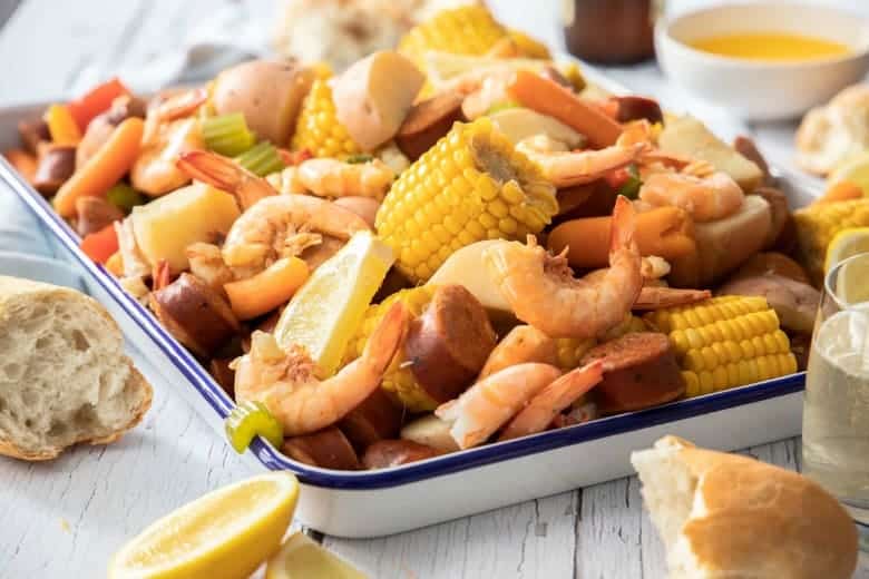 Shrimp boil recipe shown ready to eat in enamel container on wooden table.