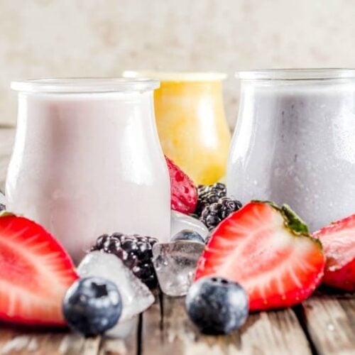 Kefir Smoothie shown in three flavors with ice, strawberries and blueberries around glass jars.