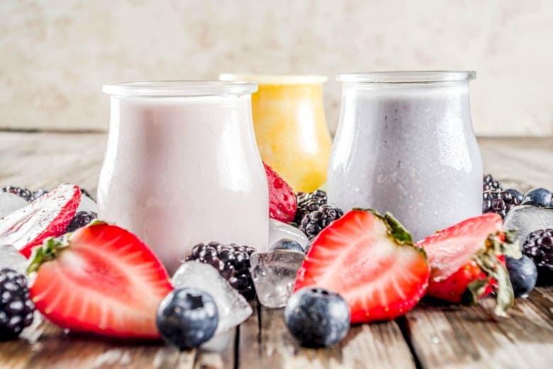 Kefir Smoothie shown in three flavors with ice, strawberries and blueberries around glass jars.