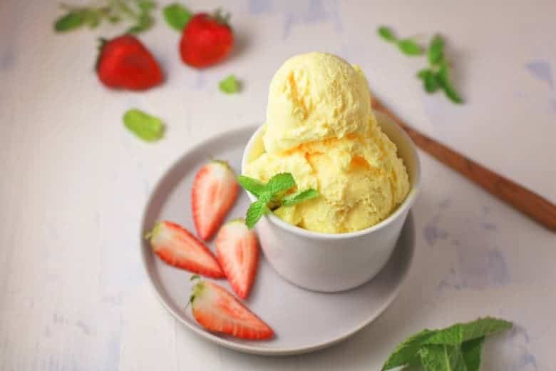 homemade vanilla ice cream served in a small white bowl with sliced strawberries and mint leaves surrounding. 