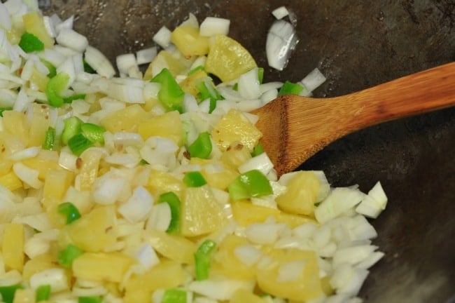 stir frying onions, peppers and pineapple to make Chinese sweet and sour stir fry