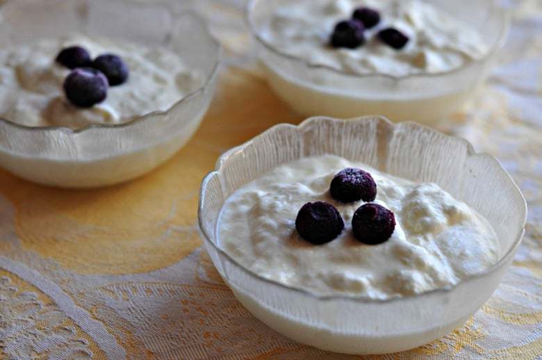 A final shot of how to make Greek yogurt showing three bowls of yogurt on a table topped with fruit