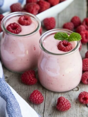 Yogurt smoothie in glass jars with raspberries and blue striped napkin.