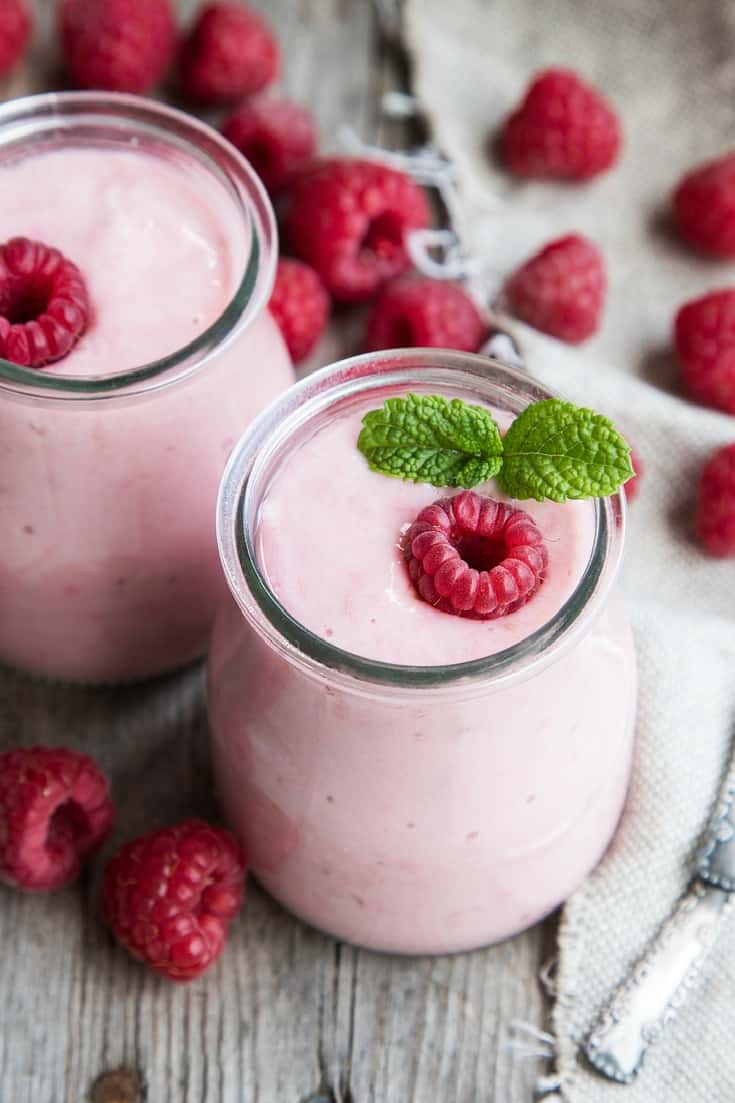 Yogurt smoothie recipe shown made in glass jars with raspberries on and around it.