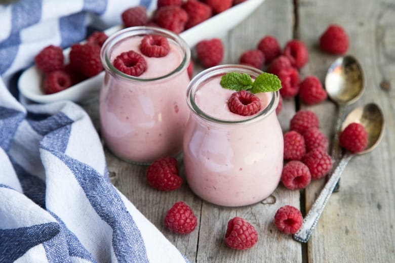 Yogurt smoothie in glass jars with raspberries and blue striped napkin.