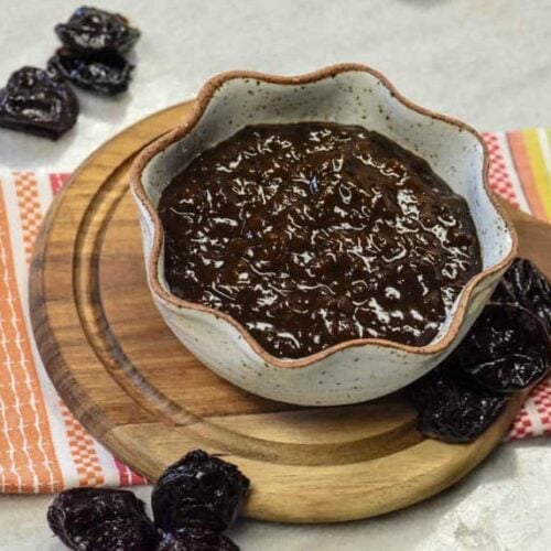 Closeup of Prune Plum Ketchup in bowl on bread board and prunes around it.