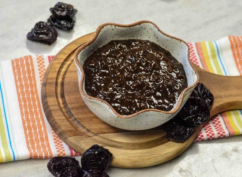 Closeup of Prune Plum Ketchup in bowl on bread board and prunes around it.