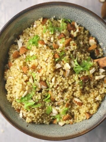 Quinoa pilaf shown in bowl with wooden spoon on cement background.