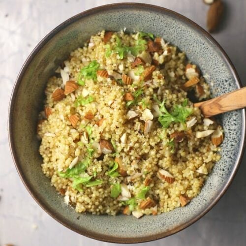 Quinoa pilaf shown in bowl with wooden spoon on cement background.