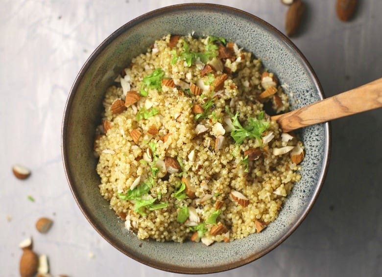 Quinoa pilaf shown in bowl with wooden spoon on cement background.