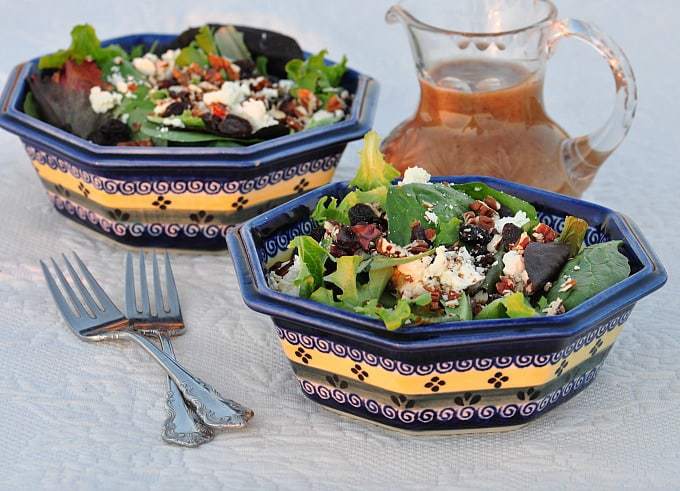 a feta salad with toasted pecan in a bowl with a vinaigrette dressing in a jug