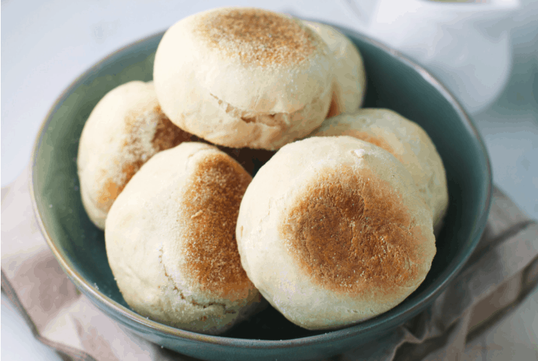 Sourdough English Muffins shown in a blue bowl on a tea towel.