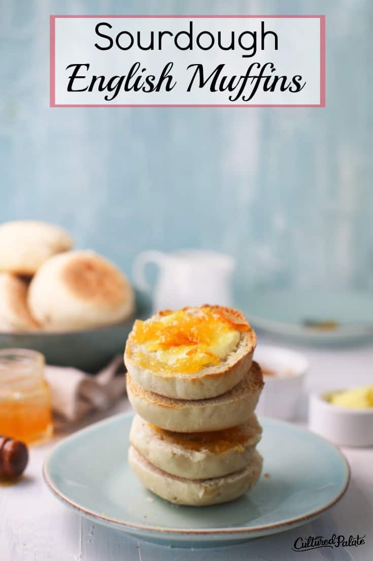 Jam covered Sourdough English Muffins shown stacked on a blue plate with a bowl of muffins in the background.