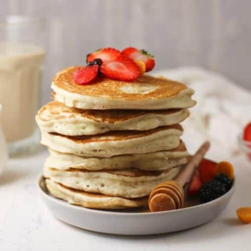 Horizontal image of Sourdough Pancakes on a white plate topped with fruit and honey.