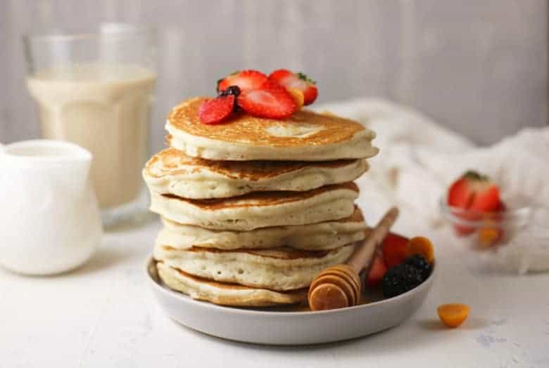 Horizontal image of Sourdough Pancakes on a white plate topped with fruit and honey.