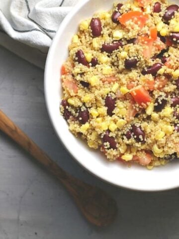 Easy Quinoa salad shown in a white bowl with wooden spoon.