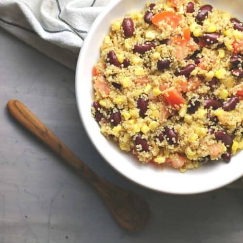 Easy Quinoa salad shown in a white bowl with wooden spoon.