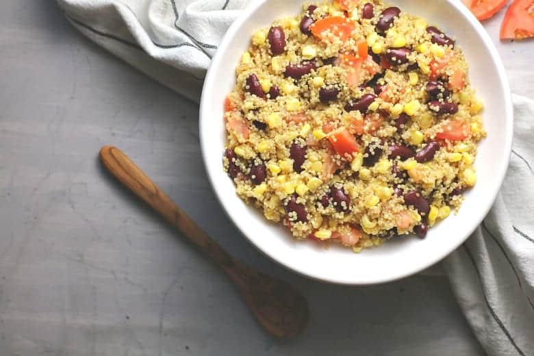 Easy Quinoa salad shown in a white bowl with wooden spoon.