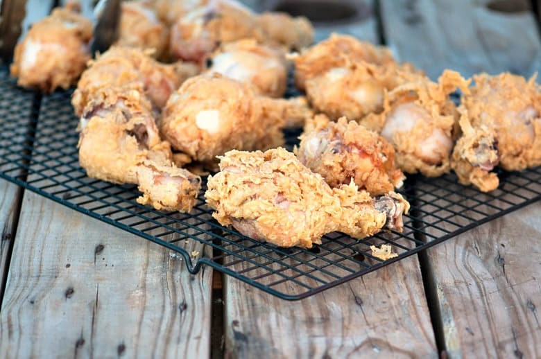A photo of fried kefir battered chicken on a draining rack sitting on a wooden surface
