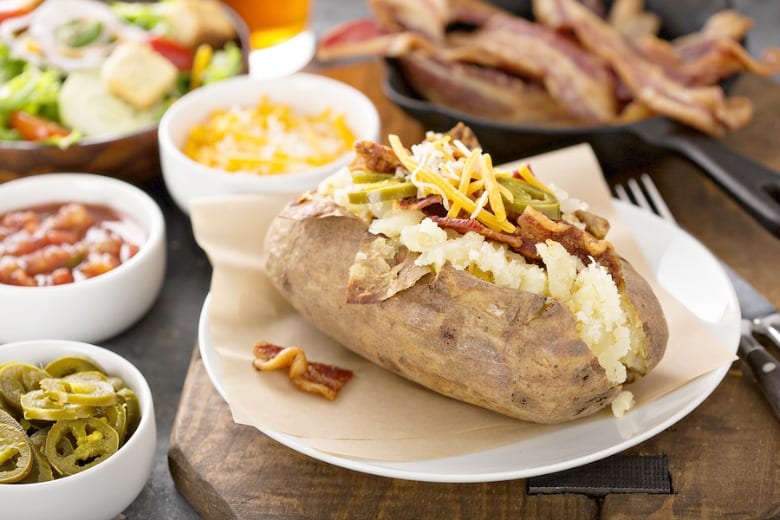 Loaded Baked Potato shown on plate with toppings in background.