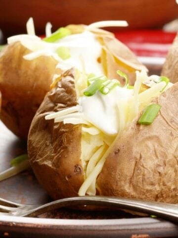 Baked Potatoes in Crock Pot shown in closeup image with fork on a plate.