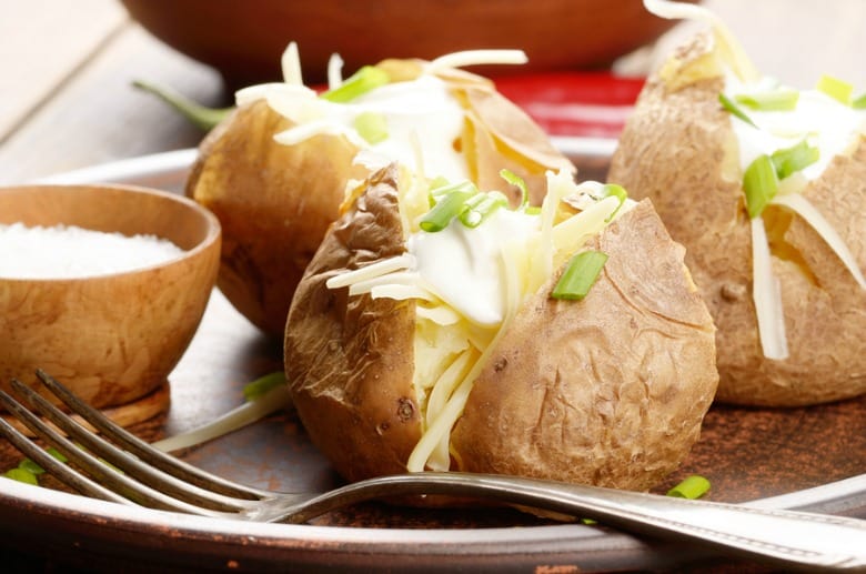 Baked Potatoes in Crock Pot shown in closeup image with fork on a plate.