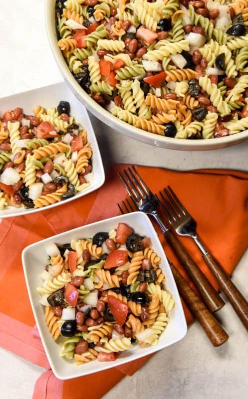 Simple Pasta Salad Recipe shown served in two white bowls and forks with serving bowl filled with salad in background