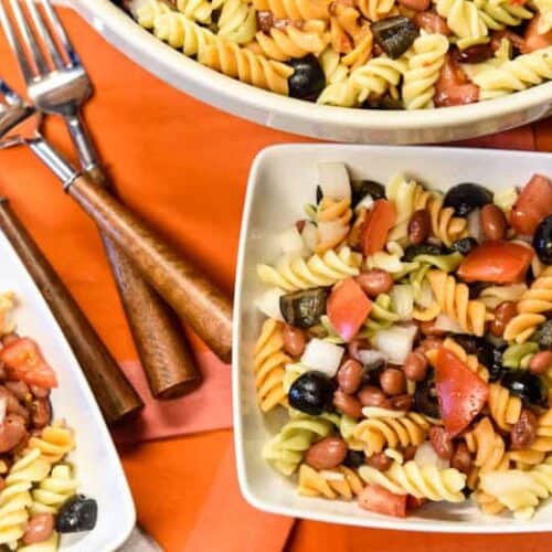 Simple Pasta Salad Recipe shown served in two white bowls and forks with serving bowl filled with salad in background